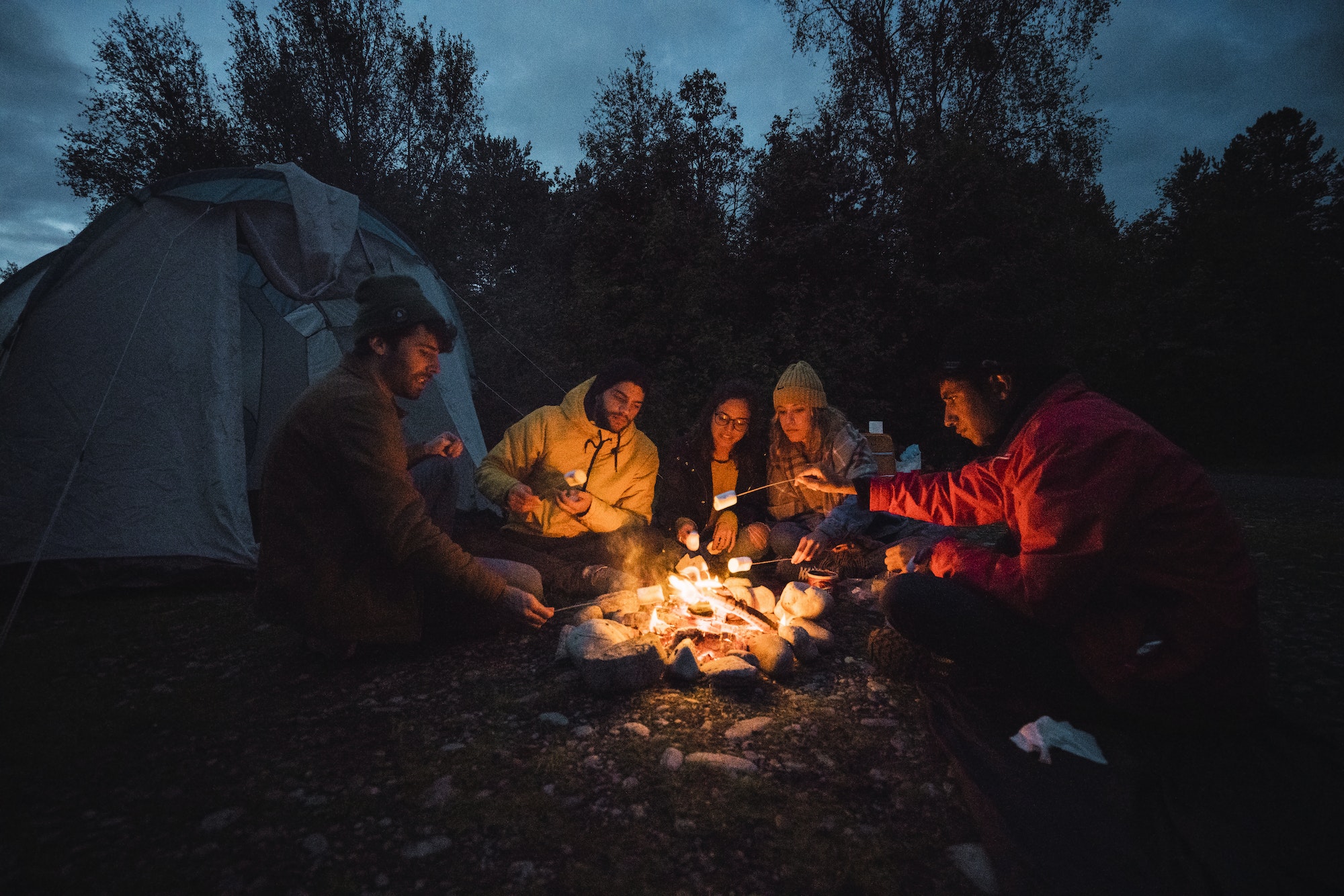 Group of friends sitting at a campfire, roasting marshmallows